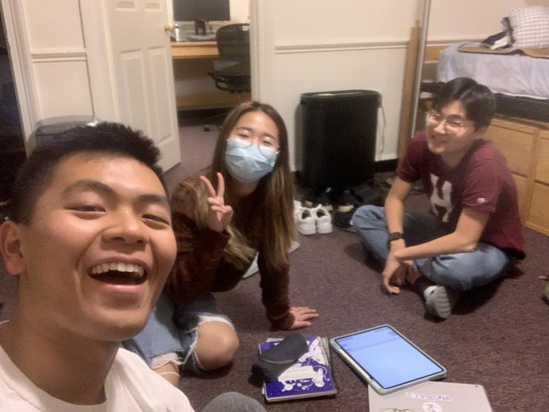Raymond, his friend, and his roommate sitting on the floor, smiling at the camera.