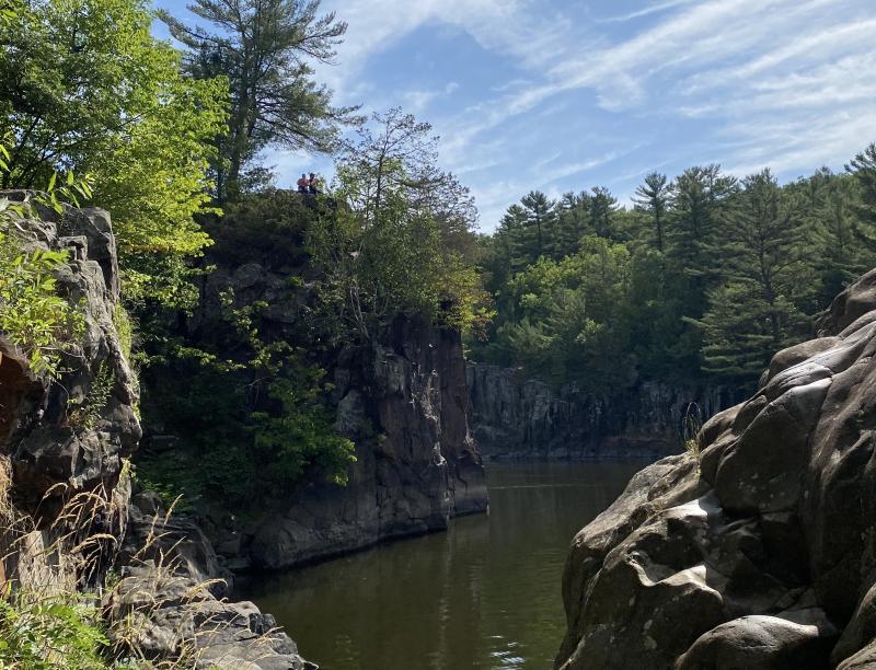 Rocky sandstone bluffs on either side of a river in the summer with green foliage. 