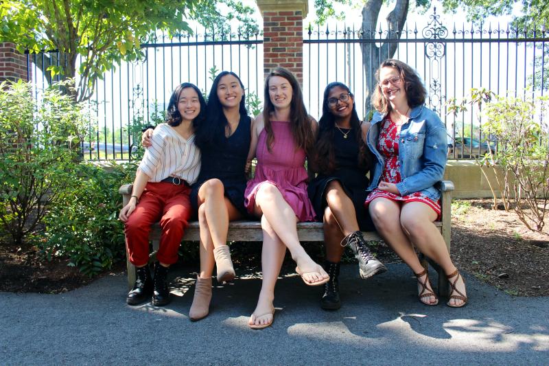 5 girls sitting together on a bench outside.