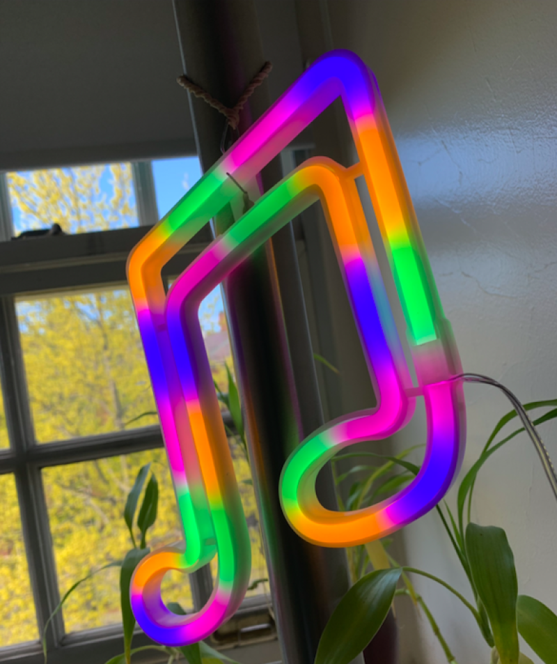 A picture of a rainbow light graphic in the shape of a music note hanging on a lamp.