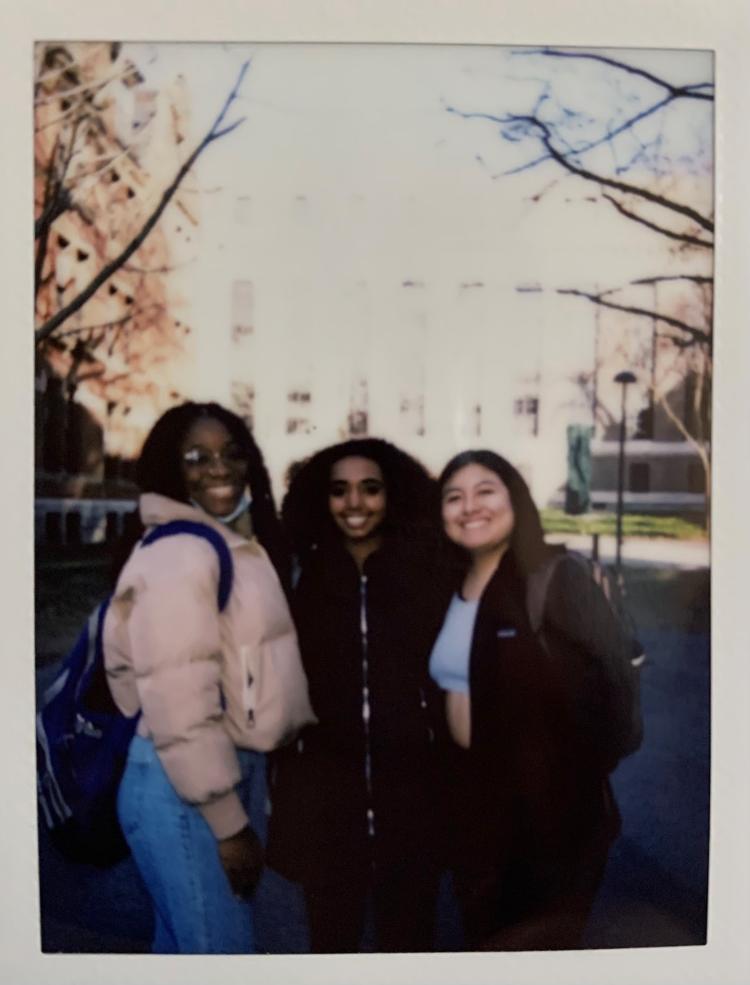 A polaroid of three girls standing by each other for in front of Harvard Yard.