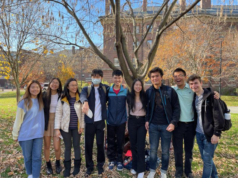 Group of students standing outside in front of a tree, smiling at the camera.