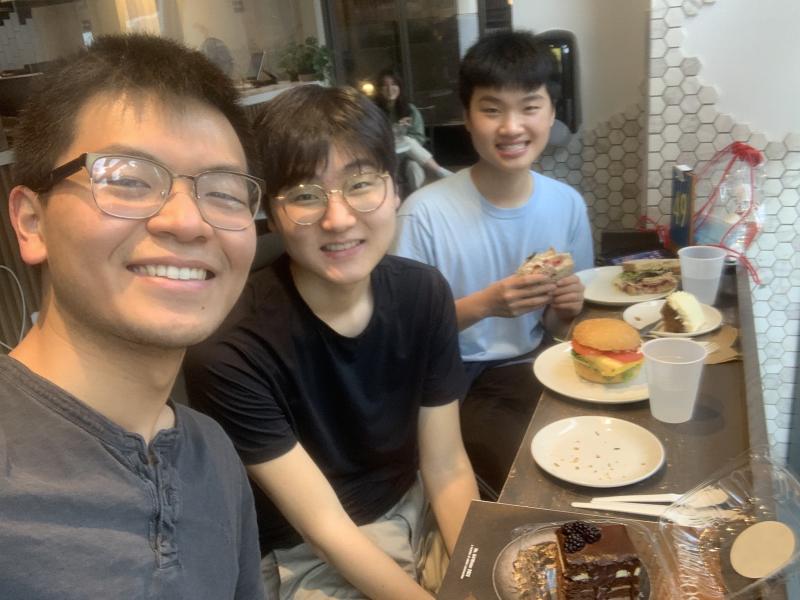 Three students sitting at a bakery with plates and a burger.