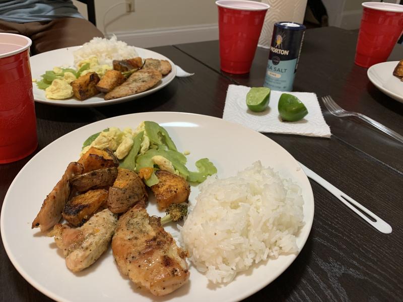 A plate with roasted chicken and vegetables, rice, and fresh greens on a table.