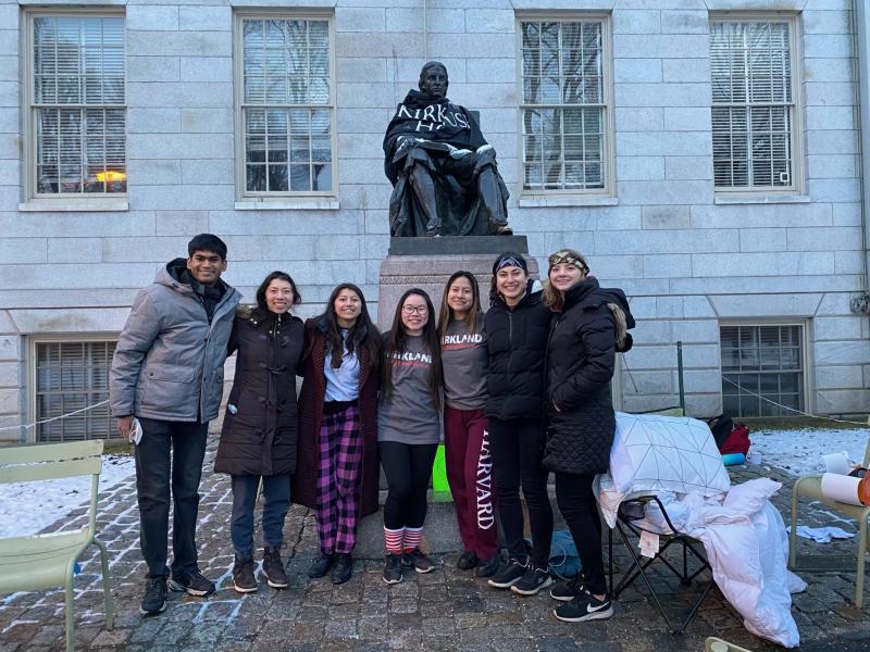 A group of Harvard students standing in front of the John Harvard Statue in Harvard Yard after spending the night outside as a part of the Black Ops for Kirkland House.