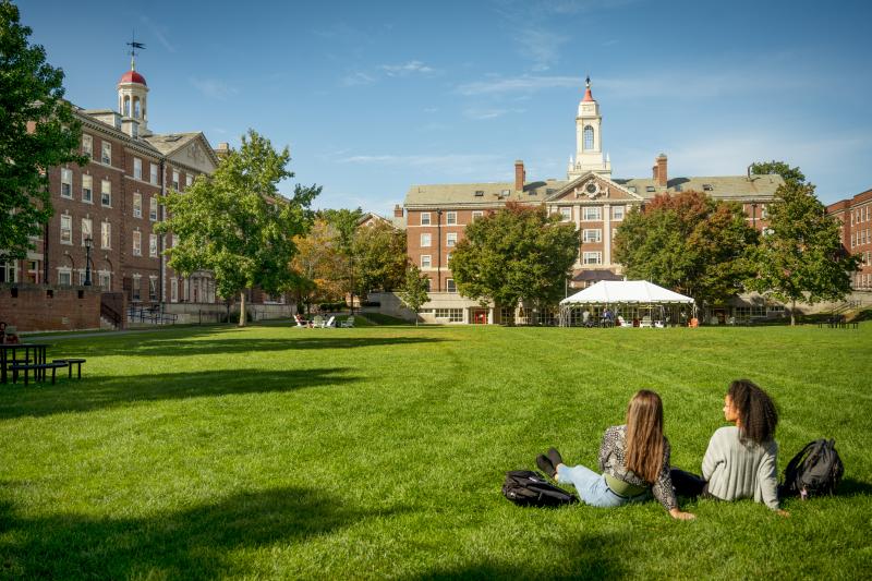 Two people sitting on a green law with a building in the distance