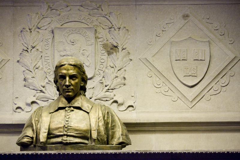 A gold statue of a man near a wall with engravings on it