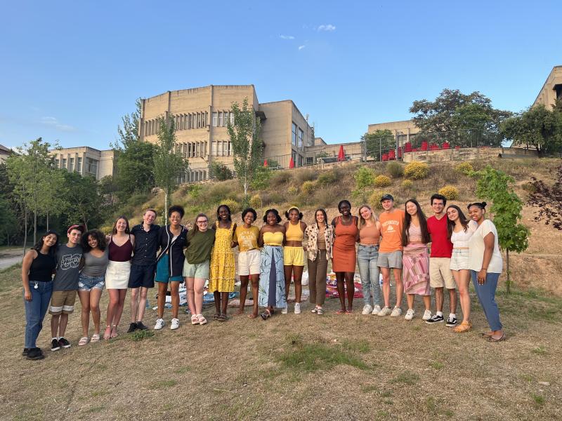 Writer and a group of around 20 students, standing in front of their residence, each wearing a different color of the rainbow