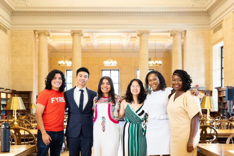 6 people stand together for a picture. They are standing in a large room and wearing formal wear. 