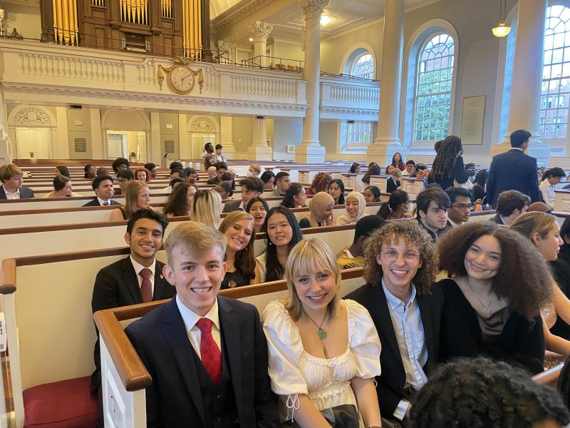 Students are sitting inside a church in formal wear. 