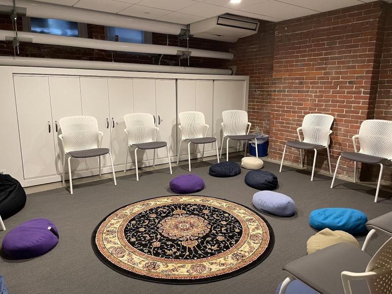 A photo of an office set up with six white chairs organized in a circle, and a rug on the floor in the middle surrounding my colorful bean bags.