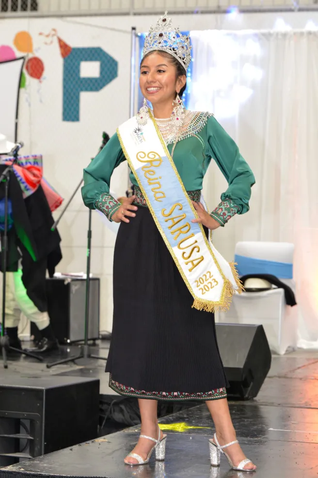 Writer posing on stage with a sash saying "Reina SARUSA"
