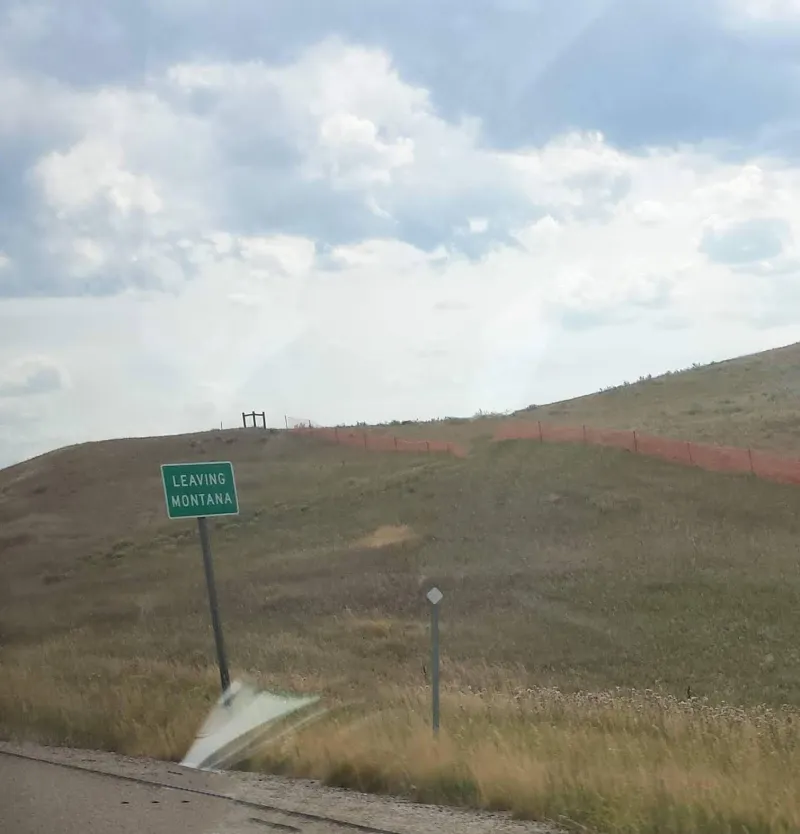 A sign saying "Leaving Montana" and green landscape behind it