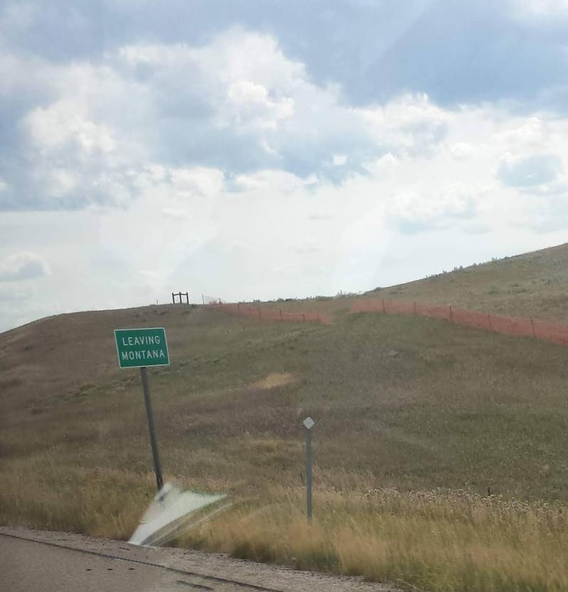 A sign saying &quot;Leaving Montana&quot; and green landscape behind it