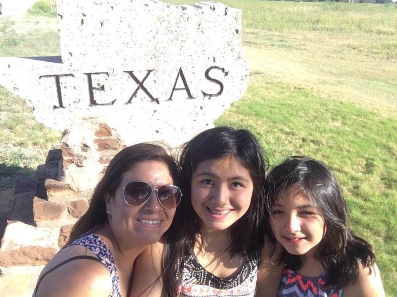 A woman and her daughters posing in front of the Texas state sign