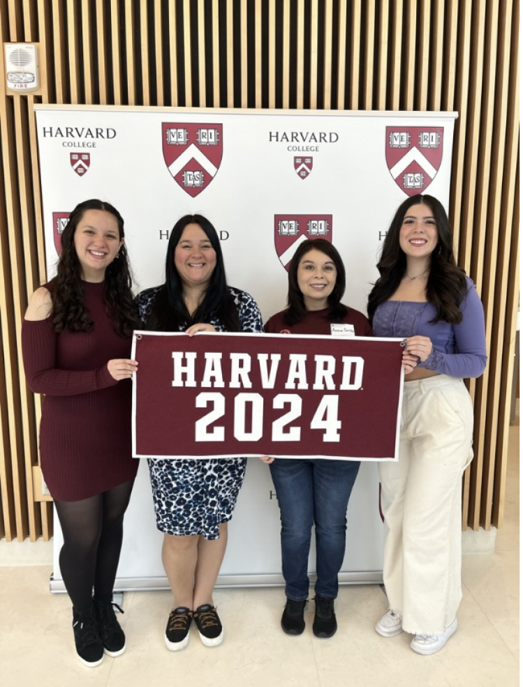 Roommates and parents smiling for a picture with a Harvard 2024 sign