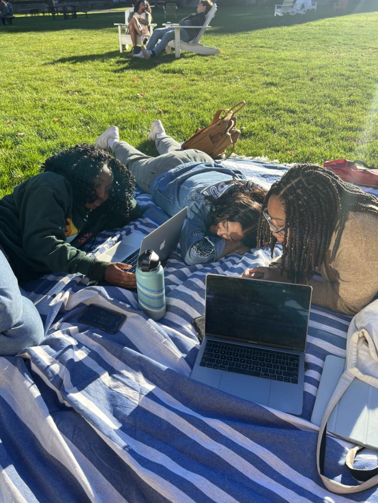 View of laptop on a picnic blanket on top of the lawn, with Harvard buildings in background