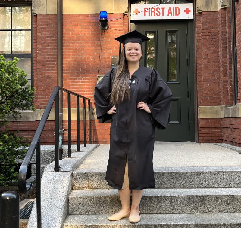 Harvard grad Perrin P standing in regalia outside Weld Hall