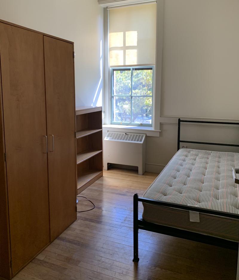 First-year dorm room with wardrobe, shelf and twin bed.
