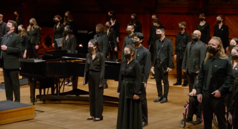 Picture of members of the Harvard-Radcliffe Collegium Musicum wearing black-colored clothing standing on stage looking out into the audience.
