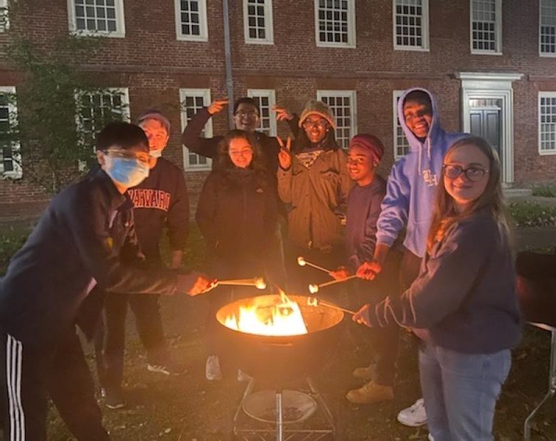 Picture of eight students standing around a fire pit roasting marshmallows and smiling at the camera.