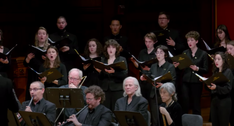 Picture of members of the Harvard-Radcliffe Collegium Musicum and an orchestra singing and playing instruments toward the camera.