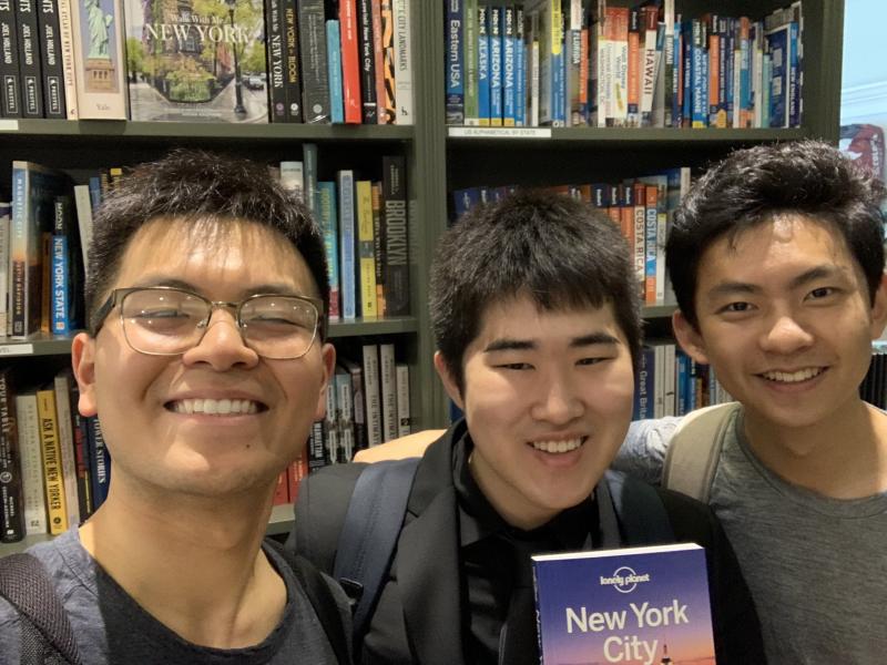 Picture of Raymond and two friends smiling in front of a row of bookshelves.
