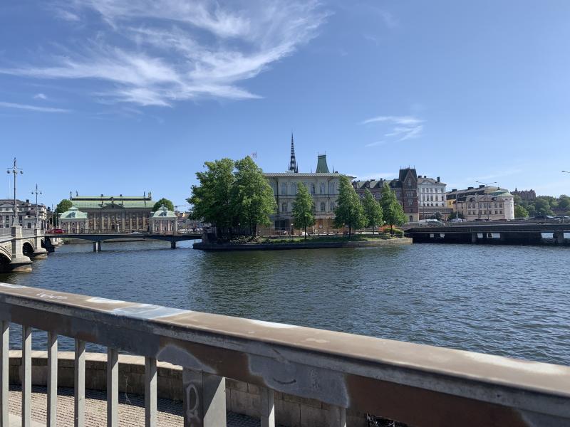 Picture of buildings in the distance above a body of water under a blue sky, taken from a bridge.