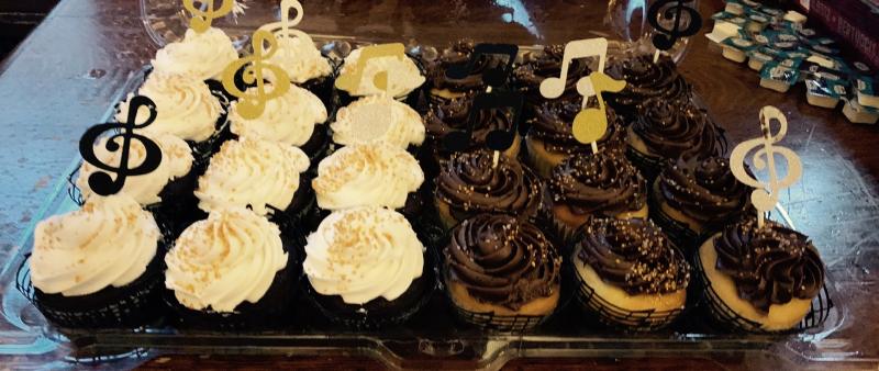 Picture of a tray of cupcakes with white and dark brown frosting and music note paper decorations on top.