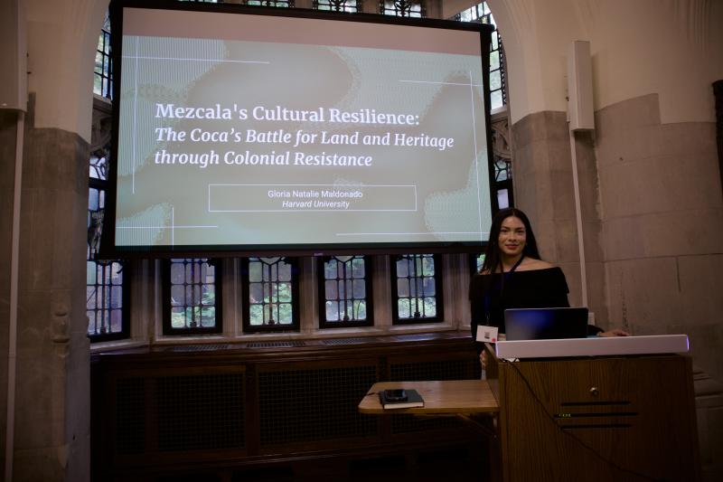 Gloria standing in front of a powerpoint which reads: "Mezcala's Cultural Resilience: The Coca's Battle for Land and Heritage through Colonial Resistance" 