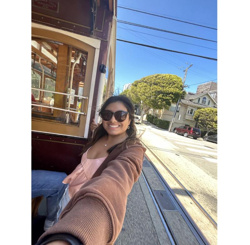 A girl taking a 0.5 picture from a San Francisco cable car, wearing sunglasses and smiling.