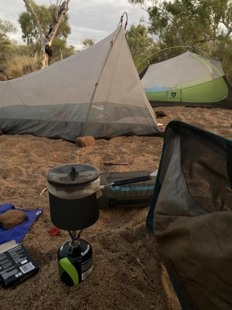 Camp in a riverbed, showing a camp stove and pot and two tents.