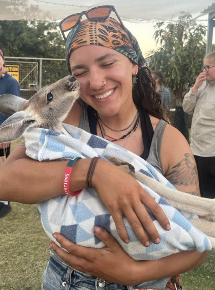Image of smiling girl (me) holding a baby kangaroo in a blanket pouch, kangaroo licking her face. 
