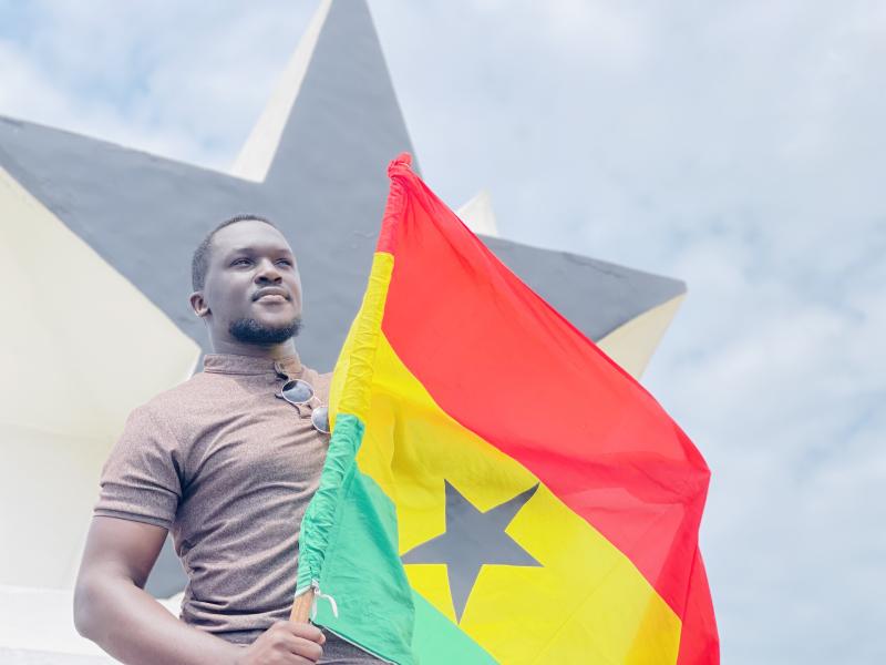 Image of author holding Ghanian Flag with a black star and the sky in the background