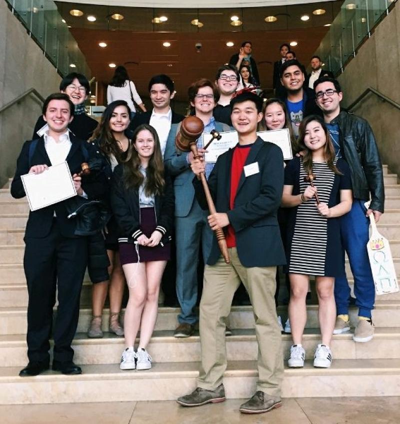 Students posing for a group photo holding certificates and a gavel