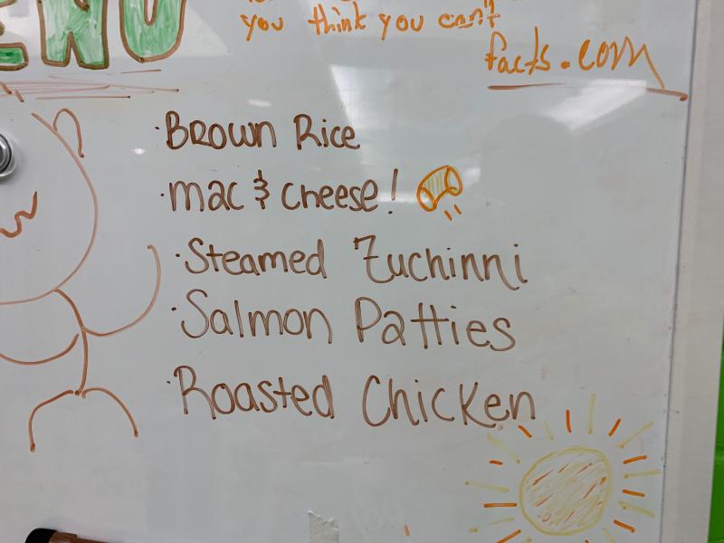 Close-up image of a white board with dinner menu items written on it.
