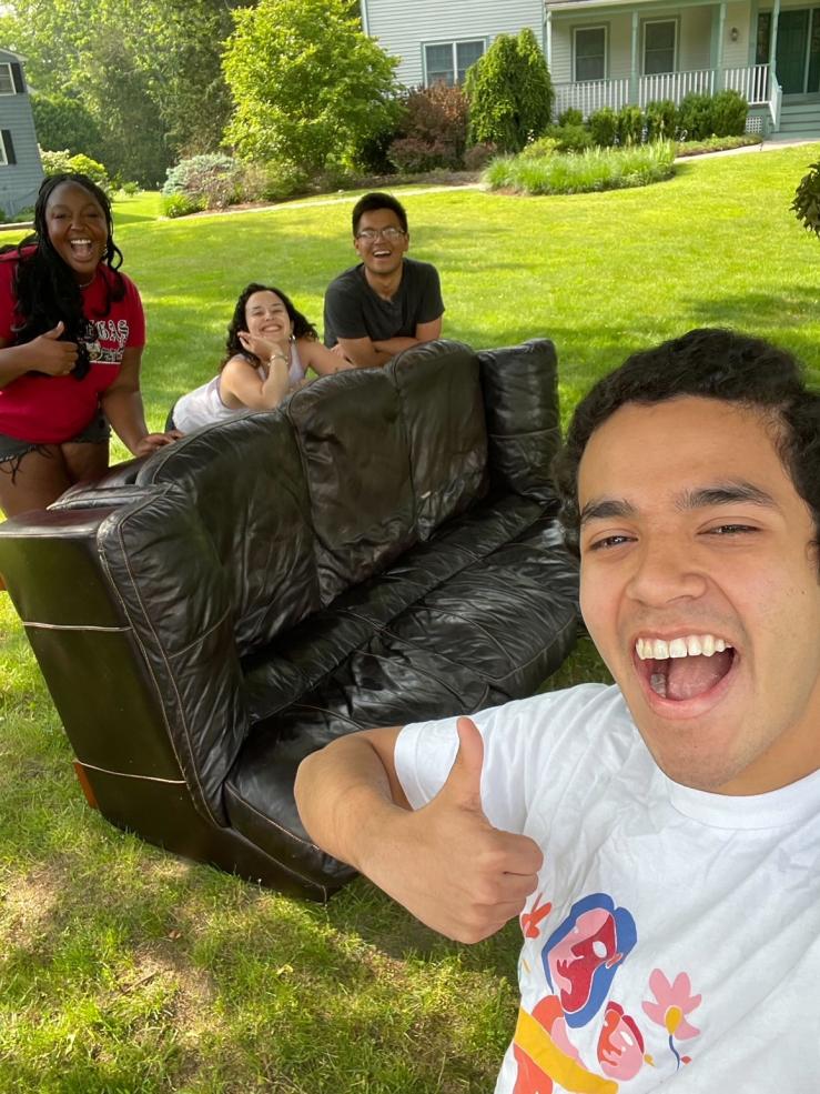 Image of people laying their arms atop a sideways-facing couch and a person in front of them smiling.