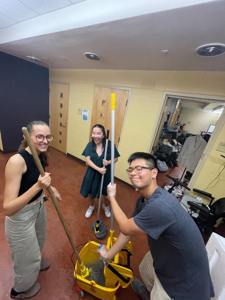 Image of three people mopping a hallway while smiling at the camera.