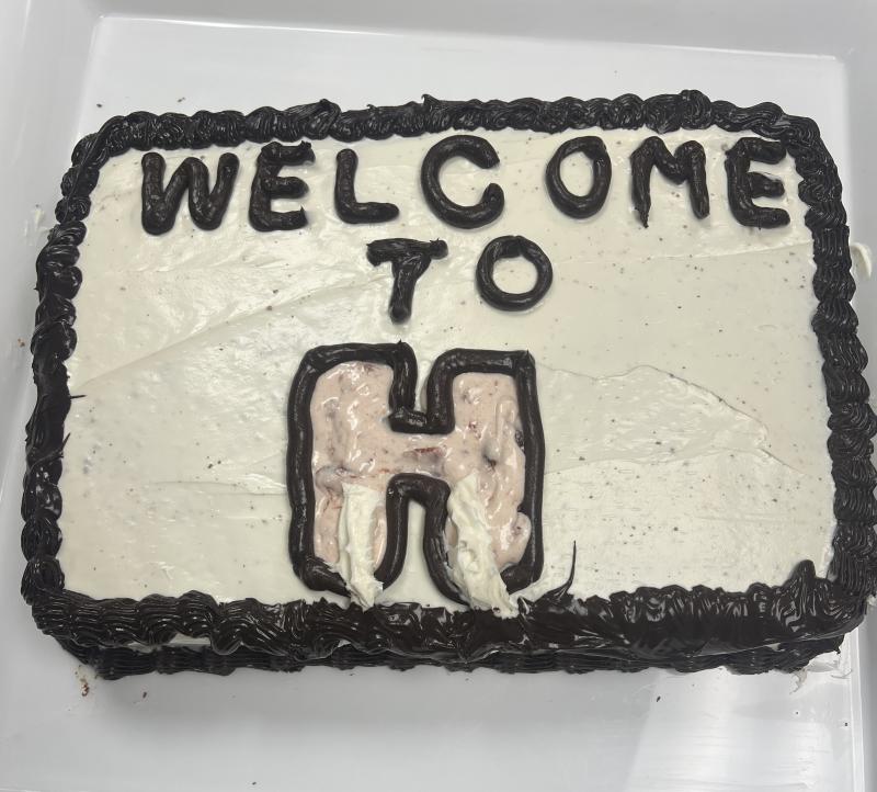 Image of a cake with white and black frosting and the words “Welcome to H” written on top.