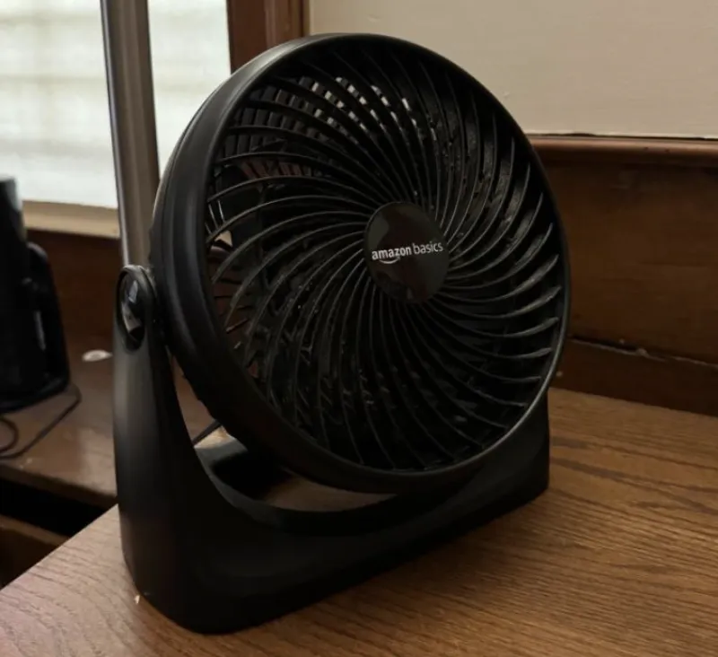 A picture of a black desk fan on top of a wooden desk.