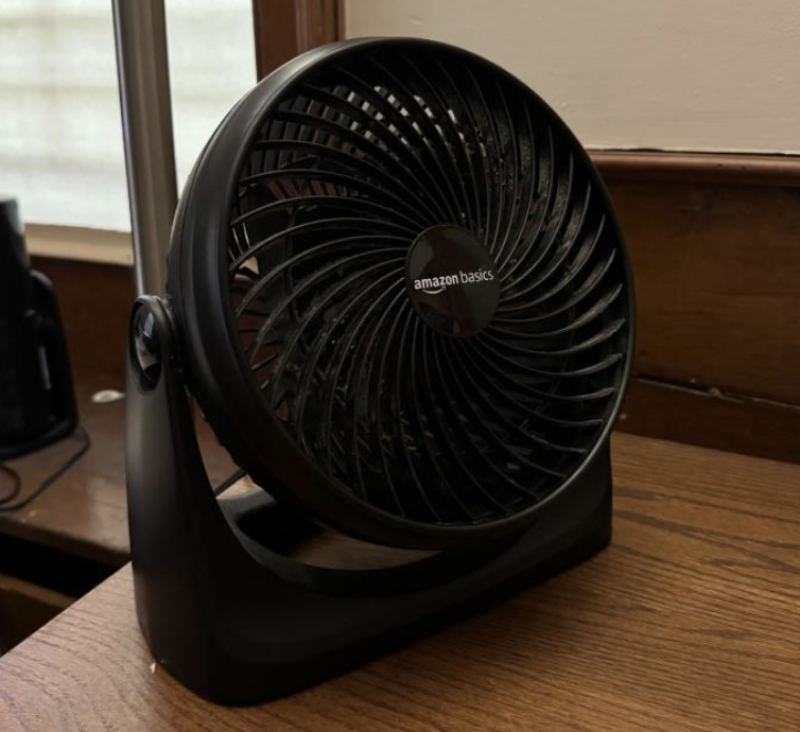 A picture of a black desk fan on top of a wooden desk.