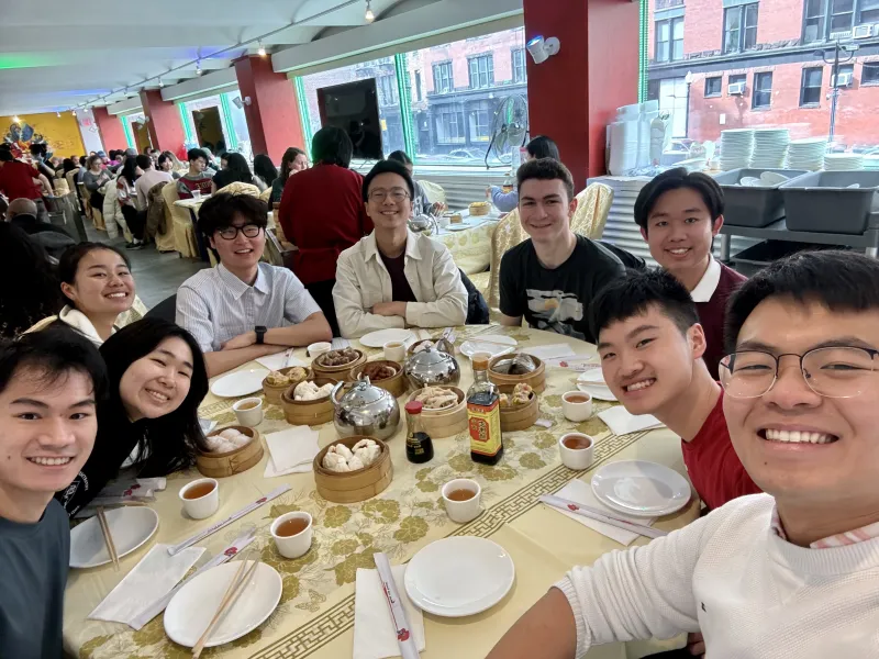 Picture of Raymond and his friends sitting around a round table in a restaurant with plates and food on the table.