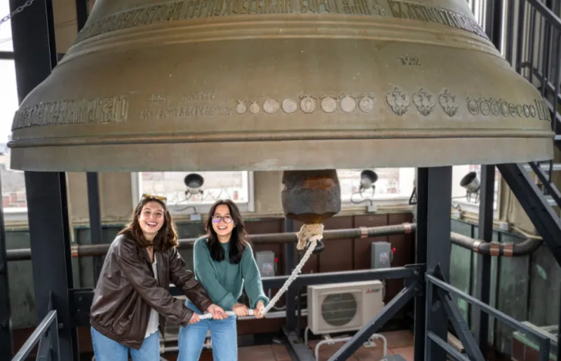 Sofia Giannuzzi (left) and Linh Vu ring a large bell in the Lowell House bell tower as part of a Sunday House tradition.
