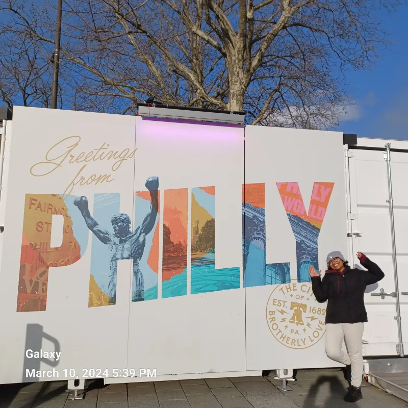 Merlin standing in front of a "Greetings from Philly" sign