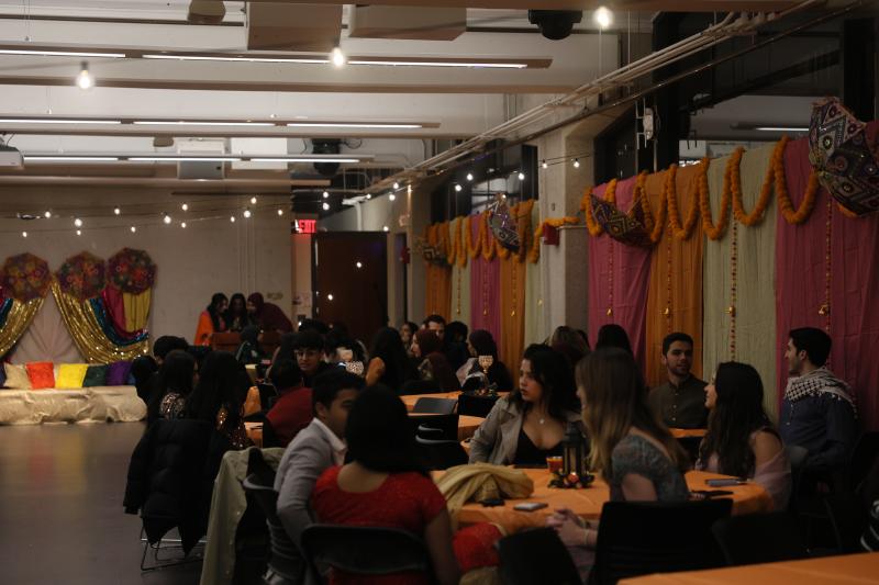 Harvard College students sitting down at round tables in a room decorated with vibrant orange, pink and yellow Pakistani decorations at event ran by Hana Rehman.