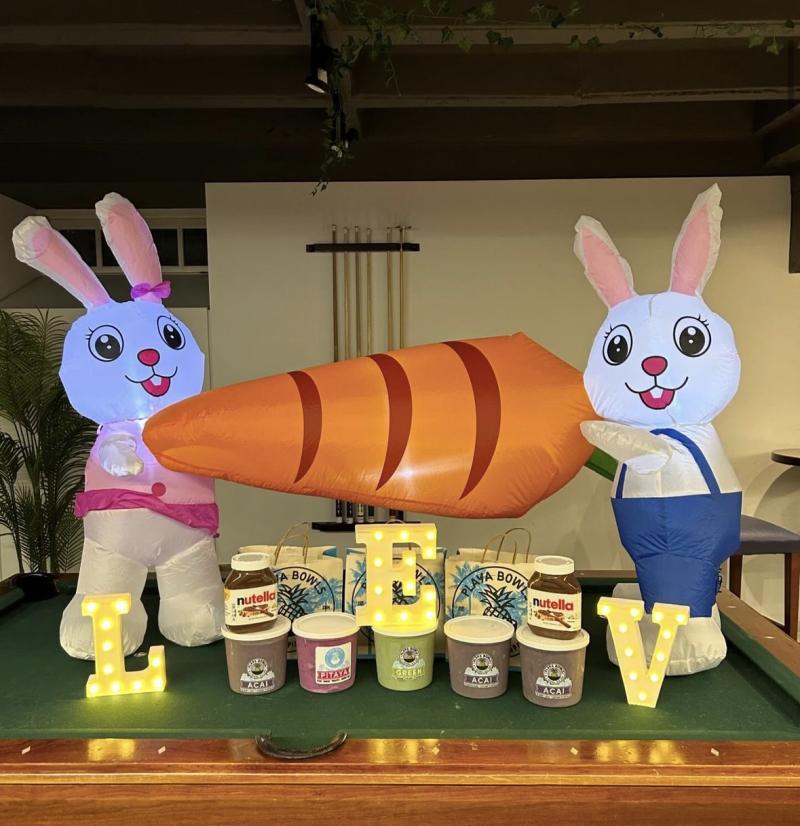 Picture of set up for Lev's Playa Bowls Stein. There are containers of acai mix on a pool table, alongside containers of nutella, and inflatable bunnies, and the words LEV in small lit up lanterns. 