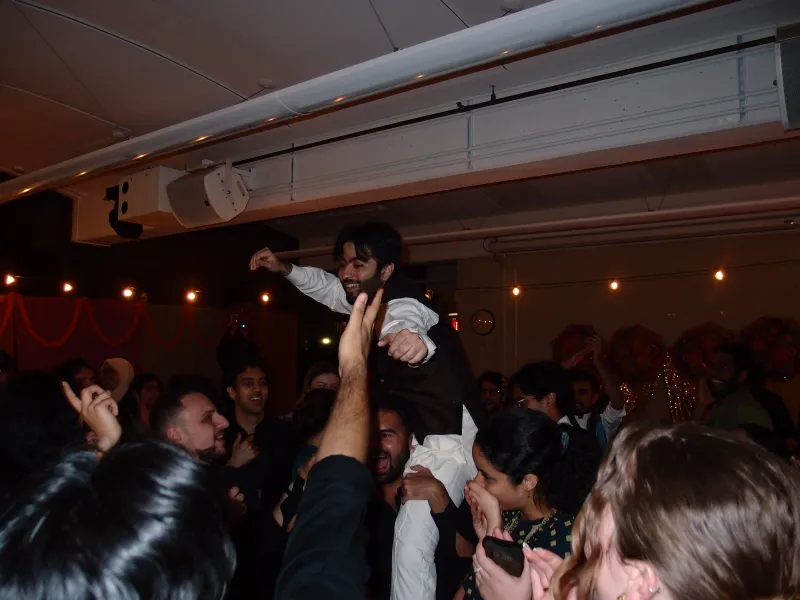 The mock groom is dancing in the open dance floor segment of the event with everyone cheering around him.