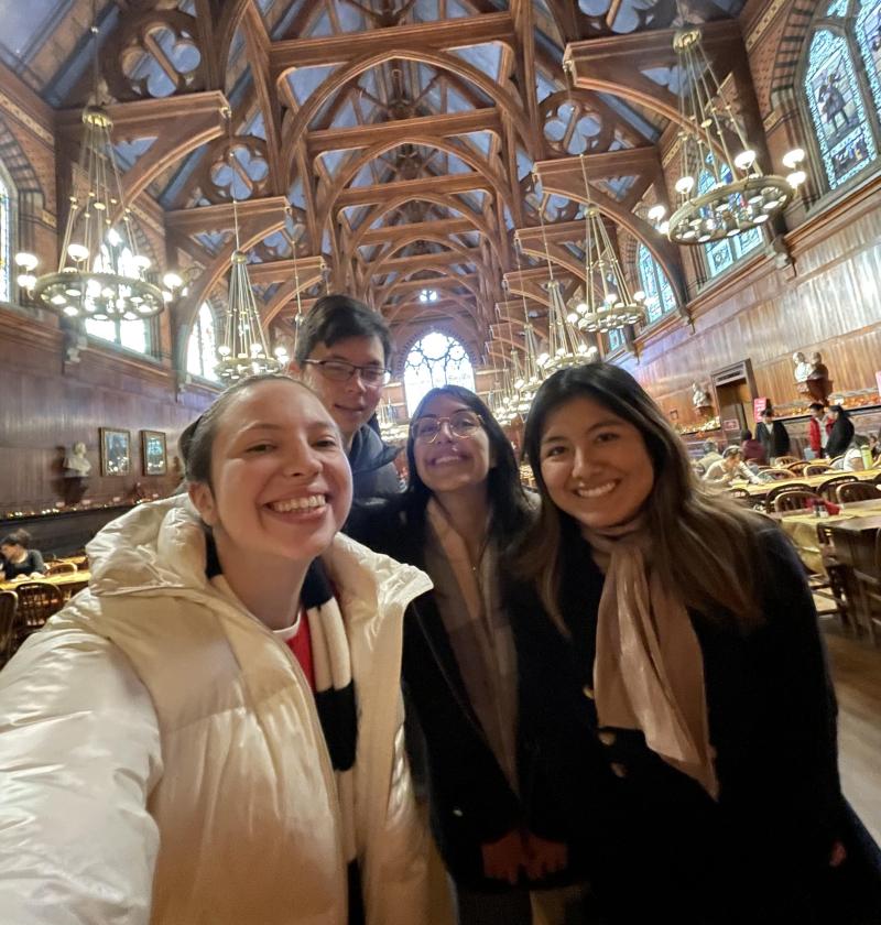 A group of four students smiling in Annenberg Hall, the first year dining hall on Harvard's campus.