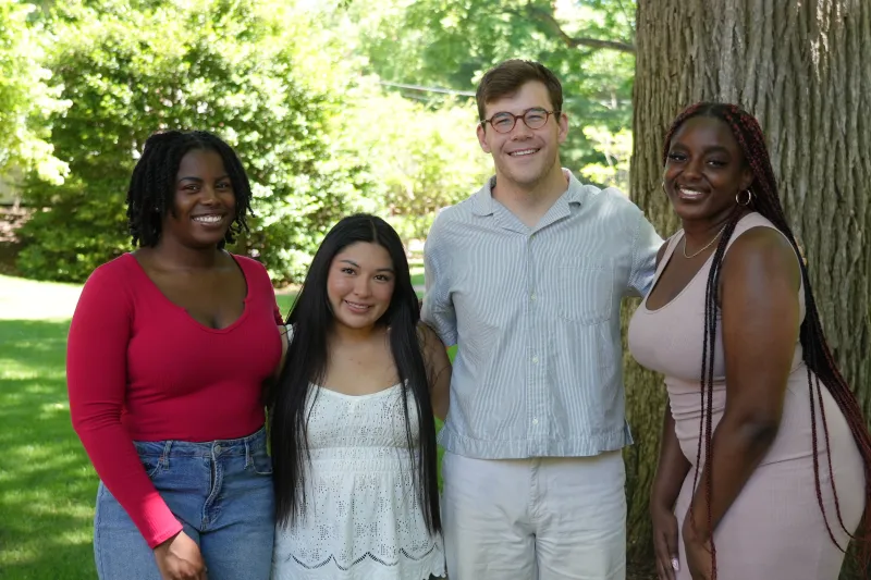A group of four students serving as Summer Student Coordinators, standing in front of a tree. 
