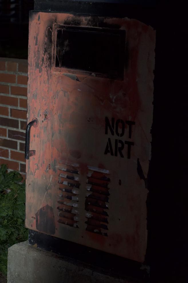 Picture of a red public mail delivery box with the words "NOT ART" painted on it. 